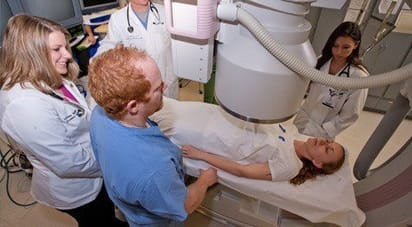 Students gathered around a woman lying underneath an x-ray machine.