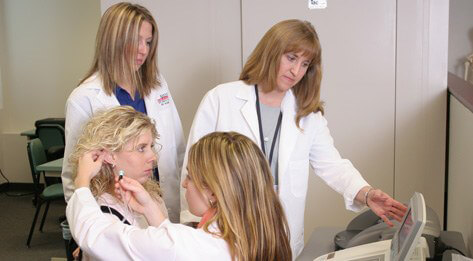 Professor and audiology students facilitating hearing test focusing on whole person healthcare.
