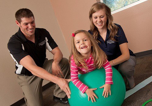 Two ATSU students with a child patient on an exercise ball