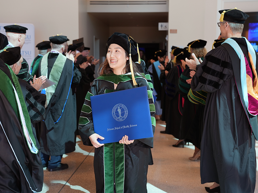 ATSU DMSc graduate walking out of the building proudly holding her diploma