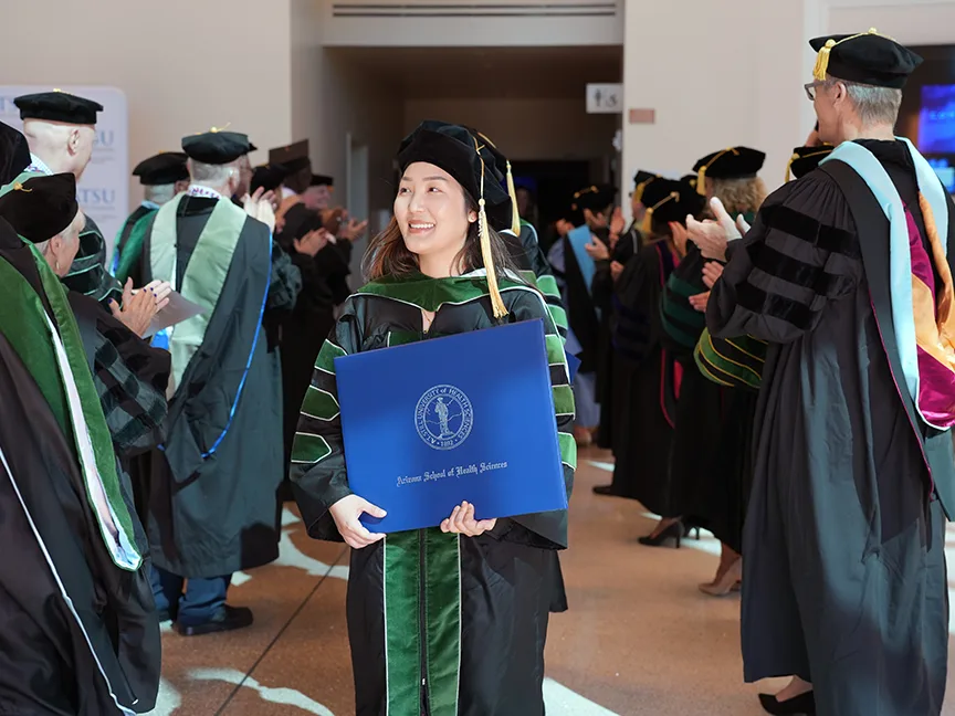 ATSU DMSc graduate walking out of the building proudly holding her diploma
