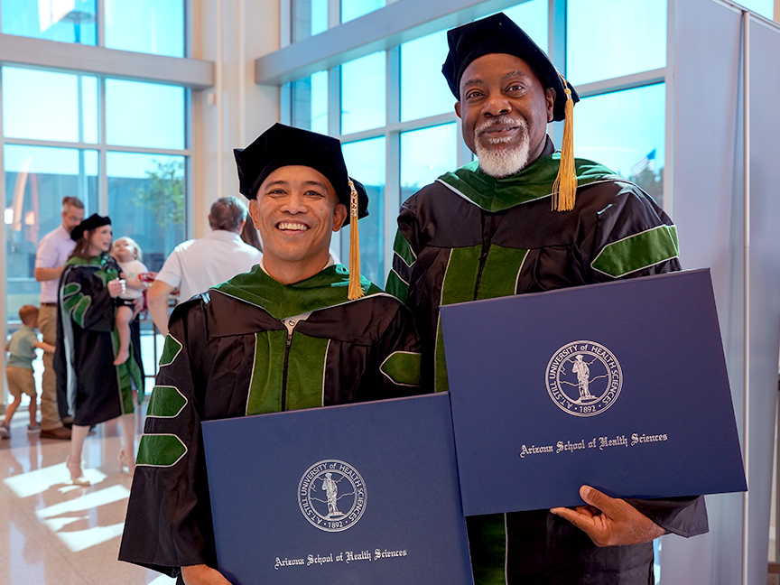 Two ATSU DMSc graduates smiling and holding their diplomas for a photo
