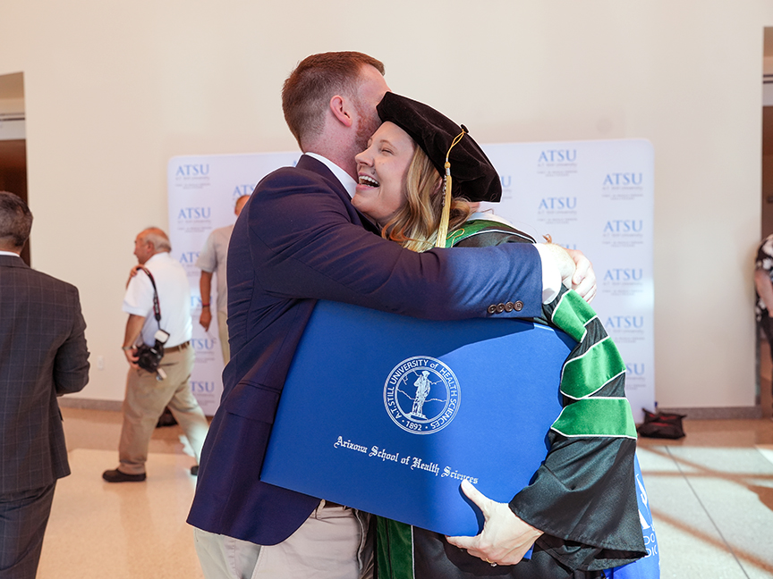 ATSU DMSc graduate holding her diploma and hugging a loved one in celebration