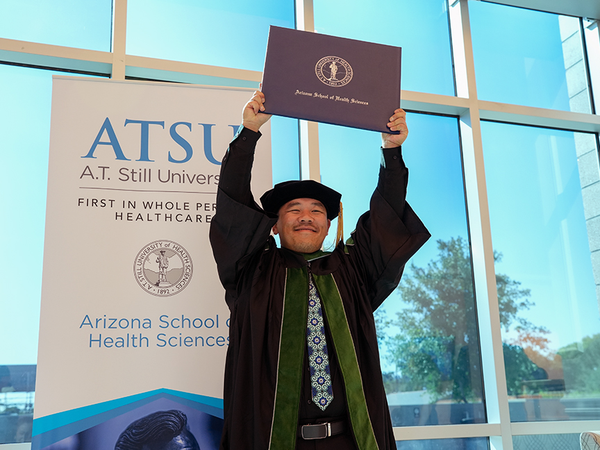 ATSU DMSc graduate smiling while proudly holding his diploma in the air