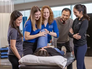 Doctor of Physical Therapy students practicing hands-on techniques, with one student lying on a table while another student stretches her leg.