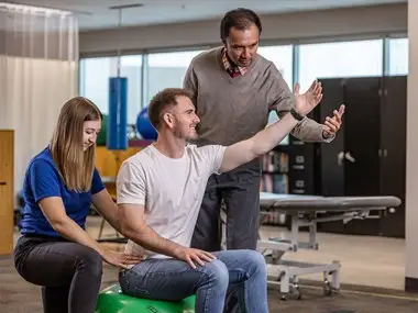 Three Doctor of Physical Therapy students practicing an arm exercise together.