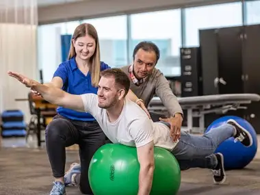 Doctor of Physical Therapy instructor guiding a DPT student as they assist another student performing an exercise on a stability ball.