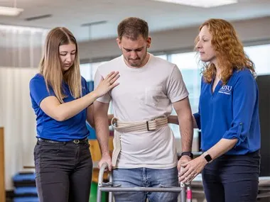 Two ATSU students assisting a patient walking with a walker.