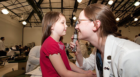 Medical professional using an ophthalmoscope to look into the eye of a young girl.