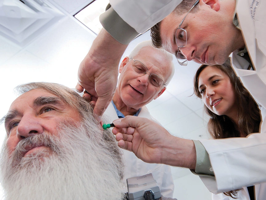 ATSU Audiology doctor examining a patient's ear with a diagnostic tool while two students observe