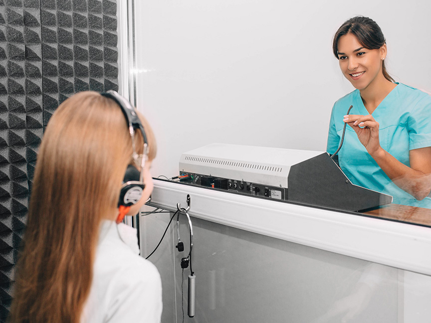 ATSU Audiology doctor conducting a hearing test on a young girl through a soundproof testing window