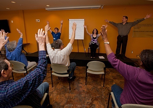 Audiology workshop featuring participants seated with their arms stretched to the sky.