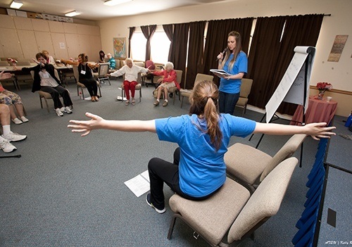Audiology student giving a presentation, featuring participants seated with their arms out like wings.
