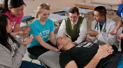 Female osteopathic medical school student practicing low amplitude osteopathic manipulative treatment (OMT) on fellow student under the supervision of a professor to emulate a patient scenario.
