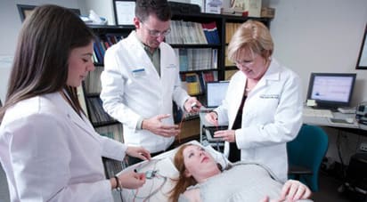 Female ATSU professor demonstrating EMG and ENG on female patient as osteopathic medical students observe.