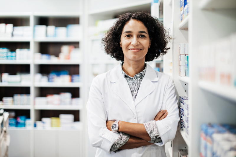 female in white coat in front of shelves of rx