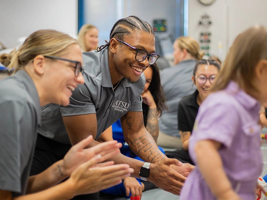 OT Students smiling as child patient succeeds in walking