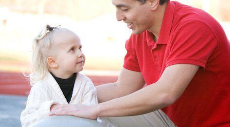 Man in a red polo smiling while talking with a young blonde girl.