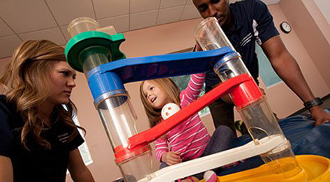 ATSU Physical Therapy students playing with a young girl in a striped pink shirt.