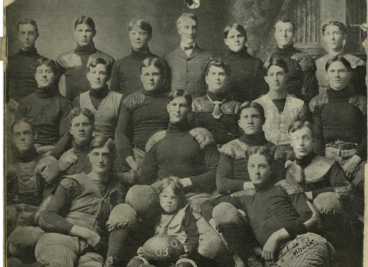 A 1903 football team picture. The group is gathered in four rows. In the center at the top row is a man in a bow tie. At the bottom of the image in the center is a child holding a ball with "A.S.O." and "03" written.
