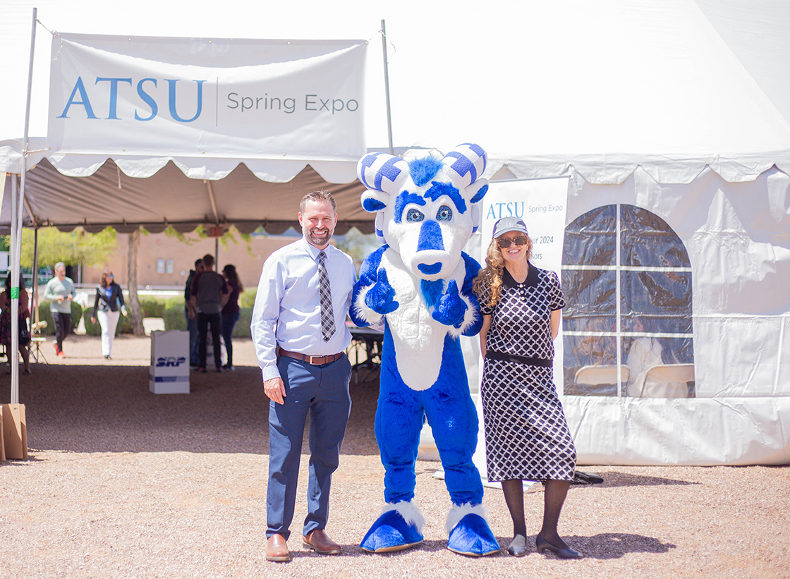 Two people stand with a mascot outside of a tented area