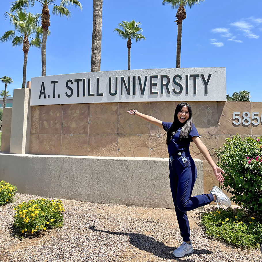 a student stands in front of the a.t. still university sign