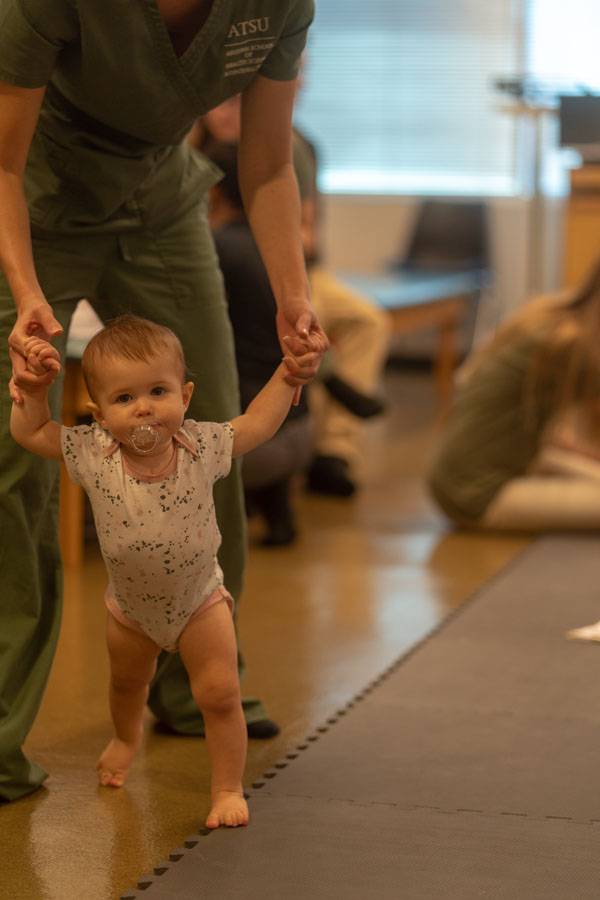 A student holds a baby's hands while they walk.