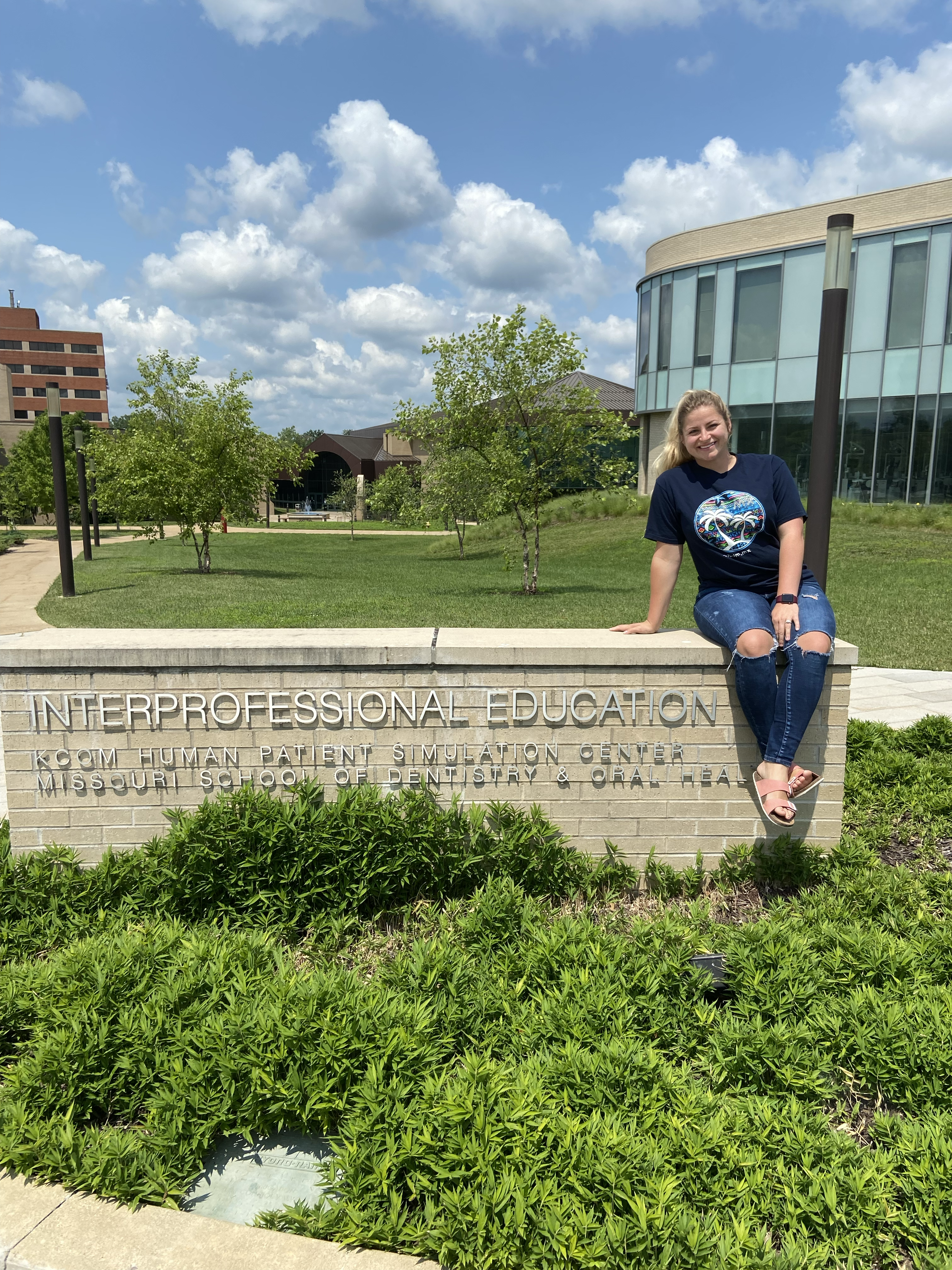 A student sits outside on a brick sign for a building on the Kirksville campus.