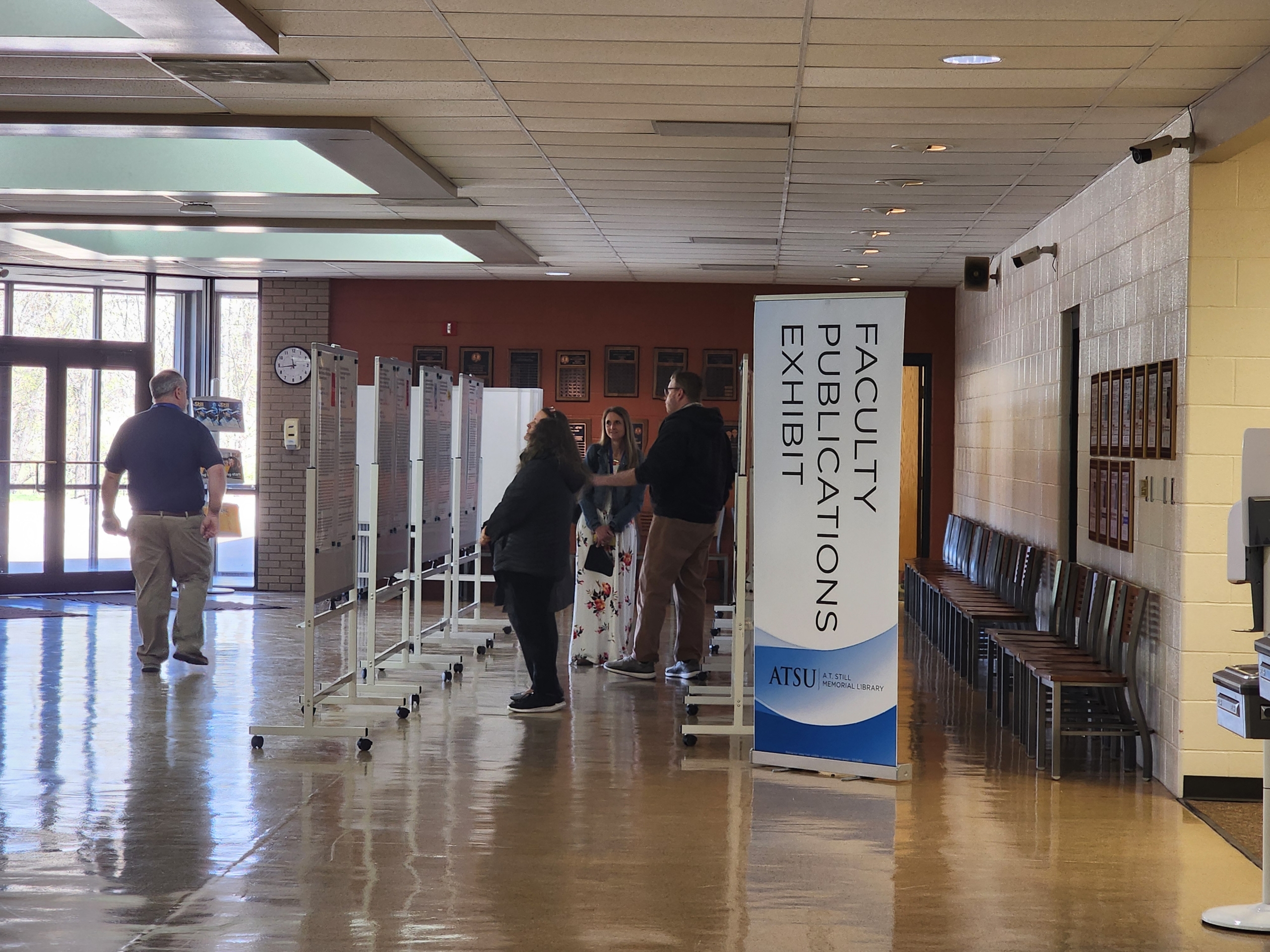 lobby space with a handful of people looking at posters - entrance to posters says “Faculty Publications Exhibit”