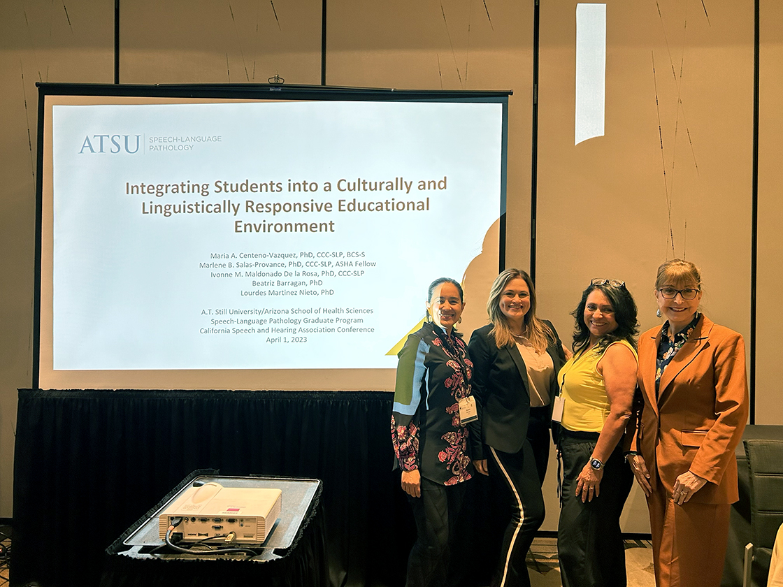 ATSU-ASHS SLP faculty stand in front of a projector screen at a conference.