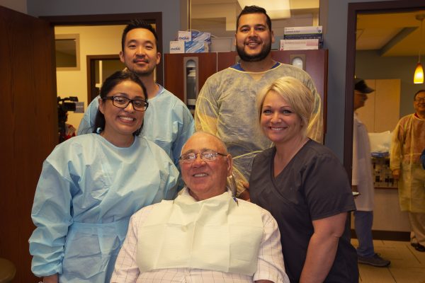 group smiling surrounding veteran with new dentures