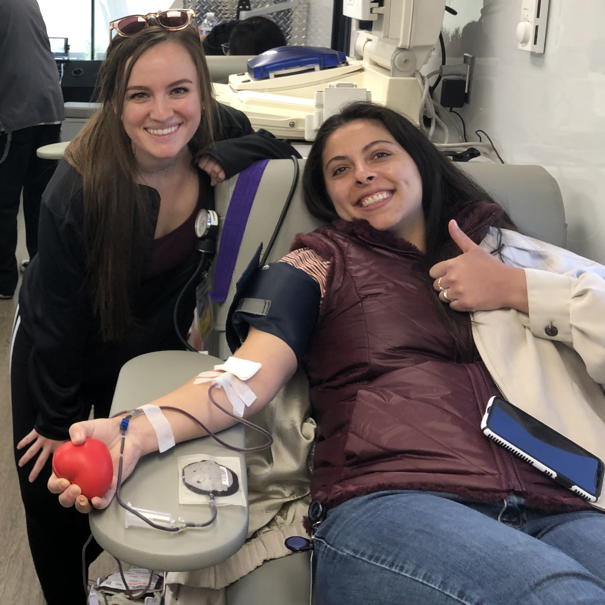 An individual donates blood, while another stands nearby.