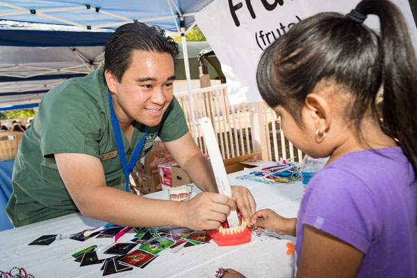 ATSU-ASDOH student Mark Vincent Donato demonstrates proper toothbrush technique on a mouth model while a young girl watches.