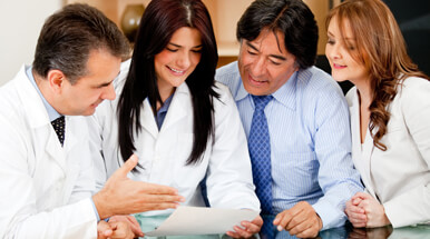 Four professionals, two of which are donning white lab coats, gazing over a piece of paper.