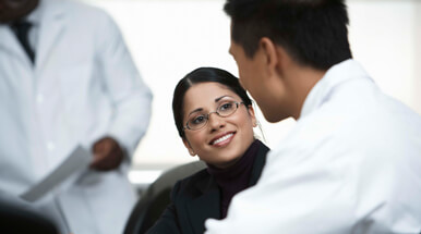 Indian woman smiling, wearing a black turtleneck and glasses.